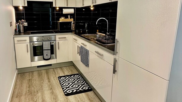 Una cocina moderna con armarios blancos, estufa de acero inoxidable y salpicadero de azulejos negros.