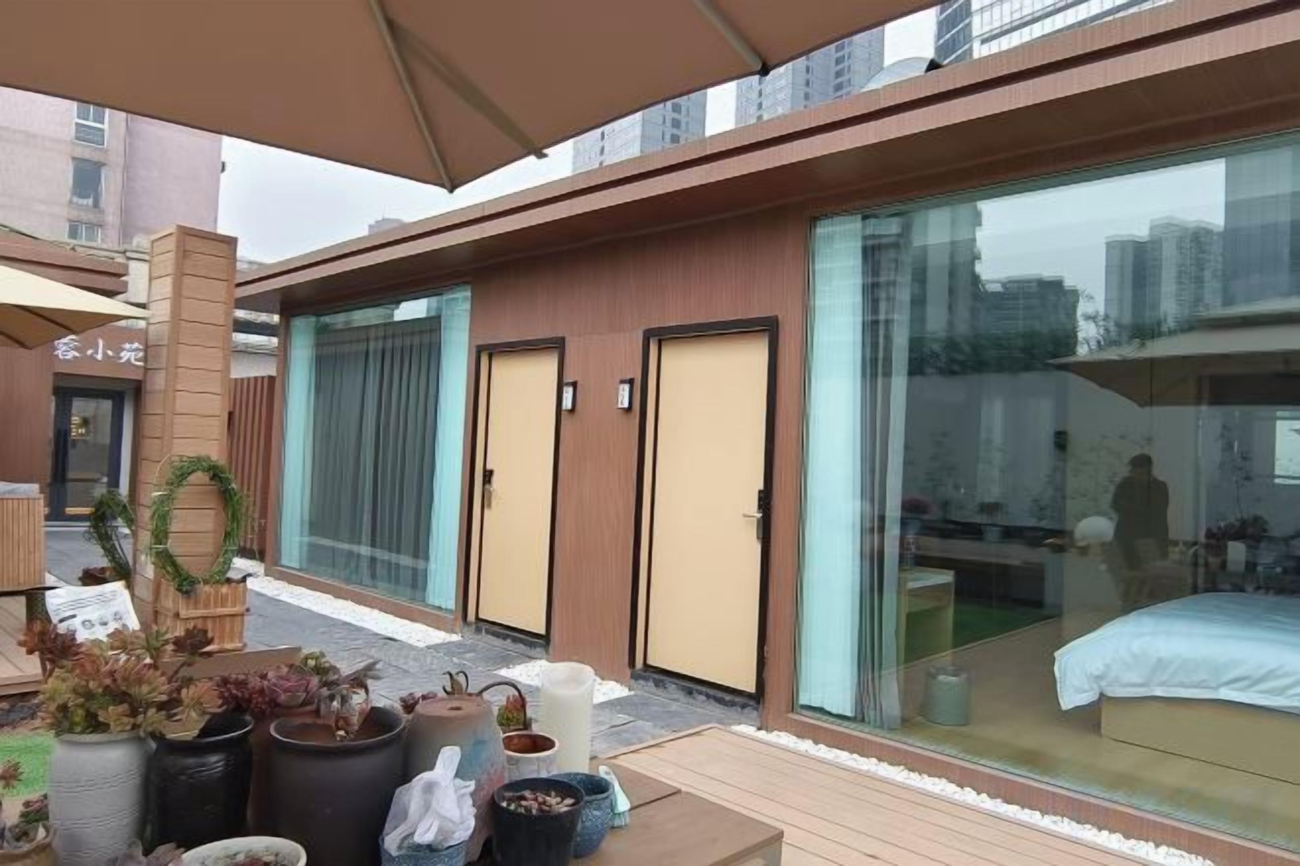 A modern hotel with a glass-enclosed room, a wooden deck with potted plants, and a large umbrella.