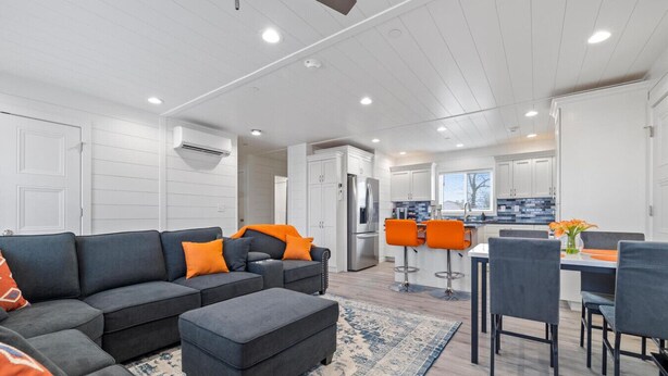 A modern living room with a sectional sofa, ottoman, and a dining area with bar stools. - UNIQUE CONTAINER HOME/Branson Landing/Trolley Stop/Gazebo (Branson)