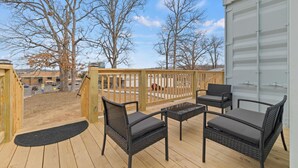 A wooden deck with wicker furniture and a view of a parking lot and buildings in the background. - UNIQUE CONTAINER HOME/Branson Landing/Trolley Stop/Gazebo (Branson)