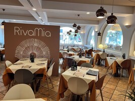 Interior de un restaurante con mesas dispuestas para comer, un llamativo letrero de 'Rivamia' y amplias ventanas que dejan entrar luz natural.