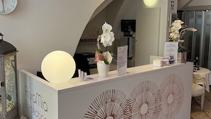 Un mostrador de recepción con un reloj, un cartel que dice "Rivamía Reception" y flores blancas decorativas.