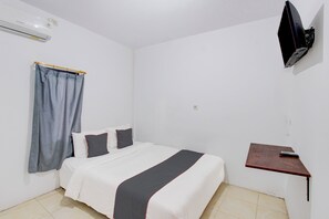 Une chambre d’hôtel avec un lit, un téléviseur fixé au mur, une petite table en bois et une fenêtre avec des rideaux.