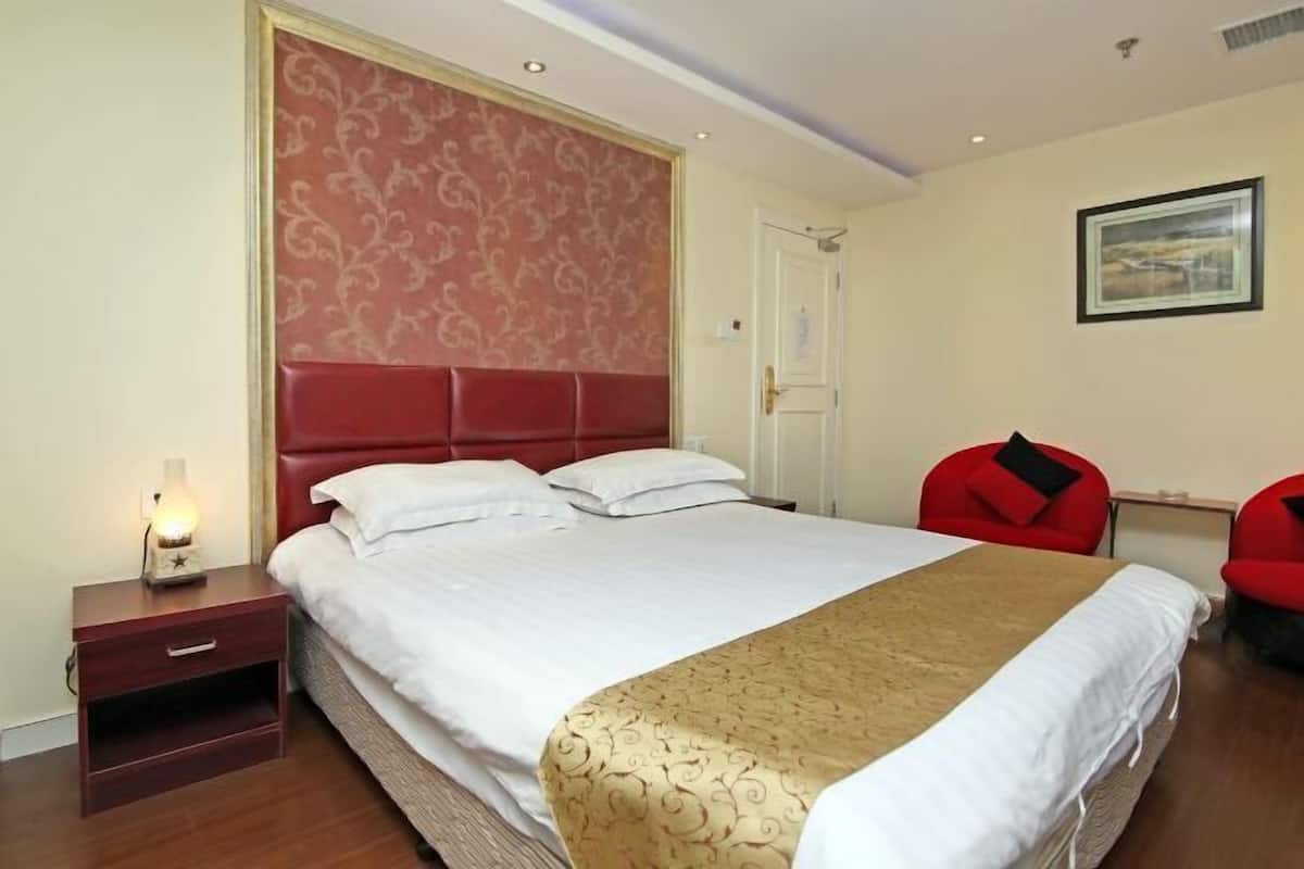 A hotel room with a bed, a nightstand, a red chair, and a framed picture on the wall.