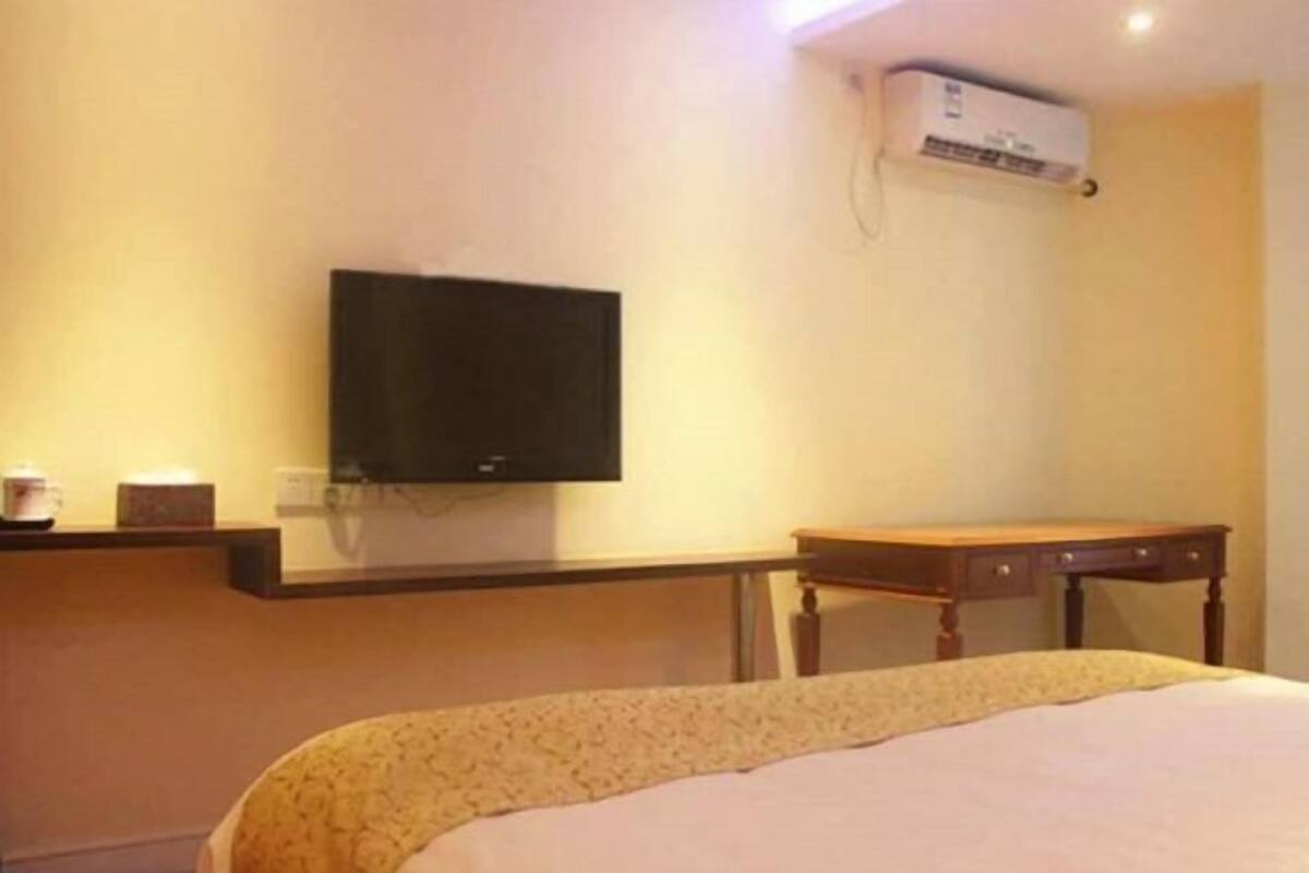 A hotel room with a bed, a flat-screen TV mounted on the wall, a small table, and a desk.