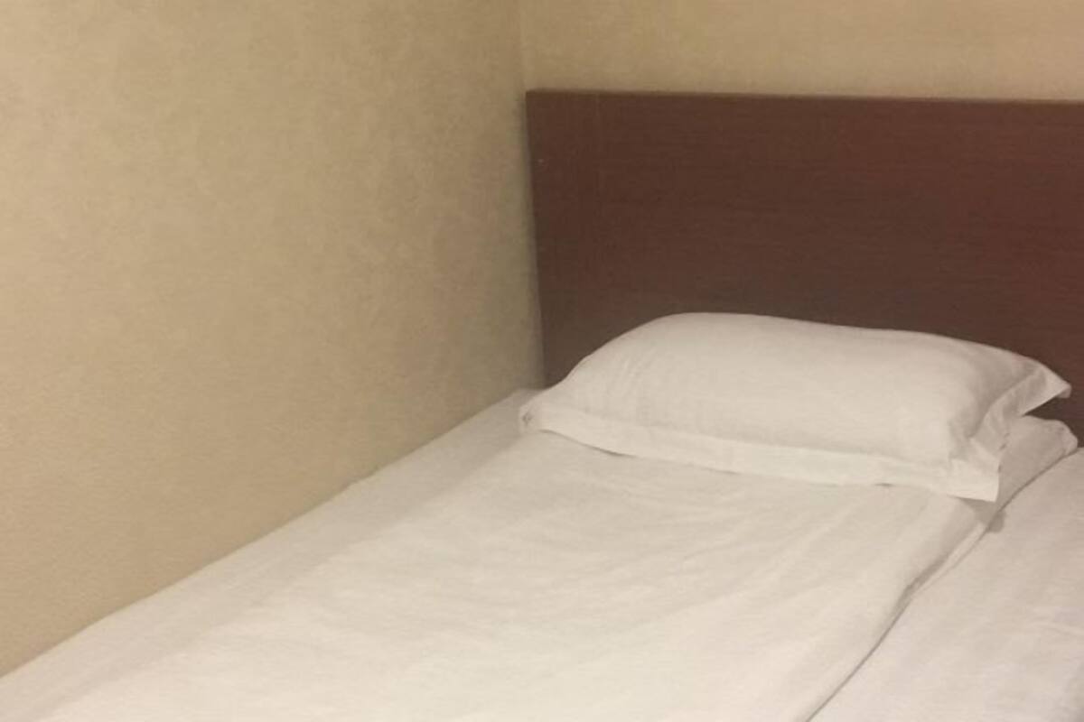 A single bed with white bedding in a room with beige walls and a brown headboard.