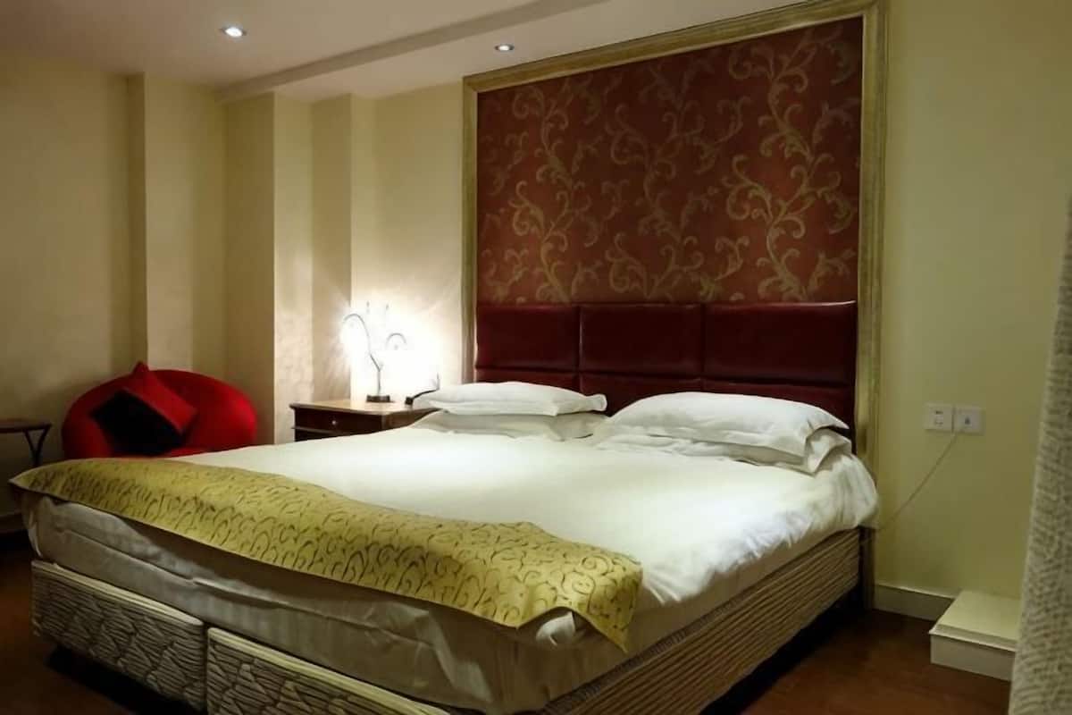 A hotel room with a large bed, a nightstand, a lamp, and a red chair.