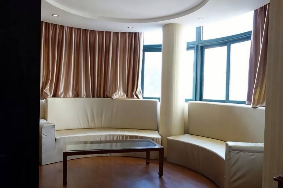 A modern living room with a curved sofa, a coffee table, and large windows with curtains.