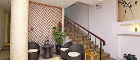 A lobby with a staircase, wicker chairs, a pillar, and a patterned wall.