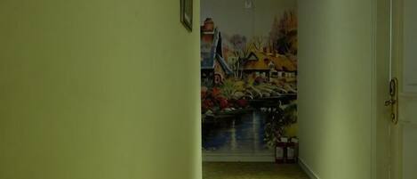 Un pasillo con un mural en la pared, una puerta a la derecha y un cuadro enmarcado a la izquierda.