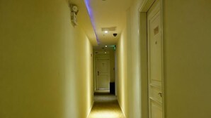 Un pasillo estrecho con suelo alfombrado, una luz en el techo y una puerta al final.