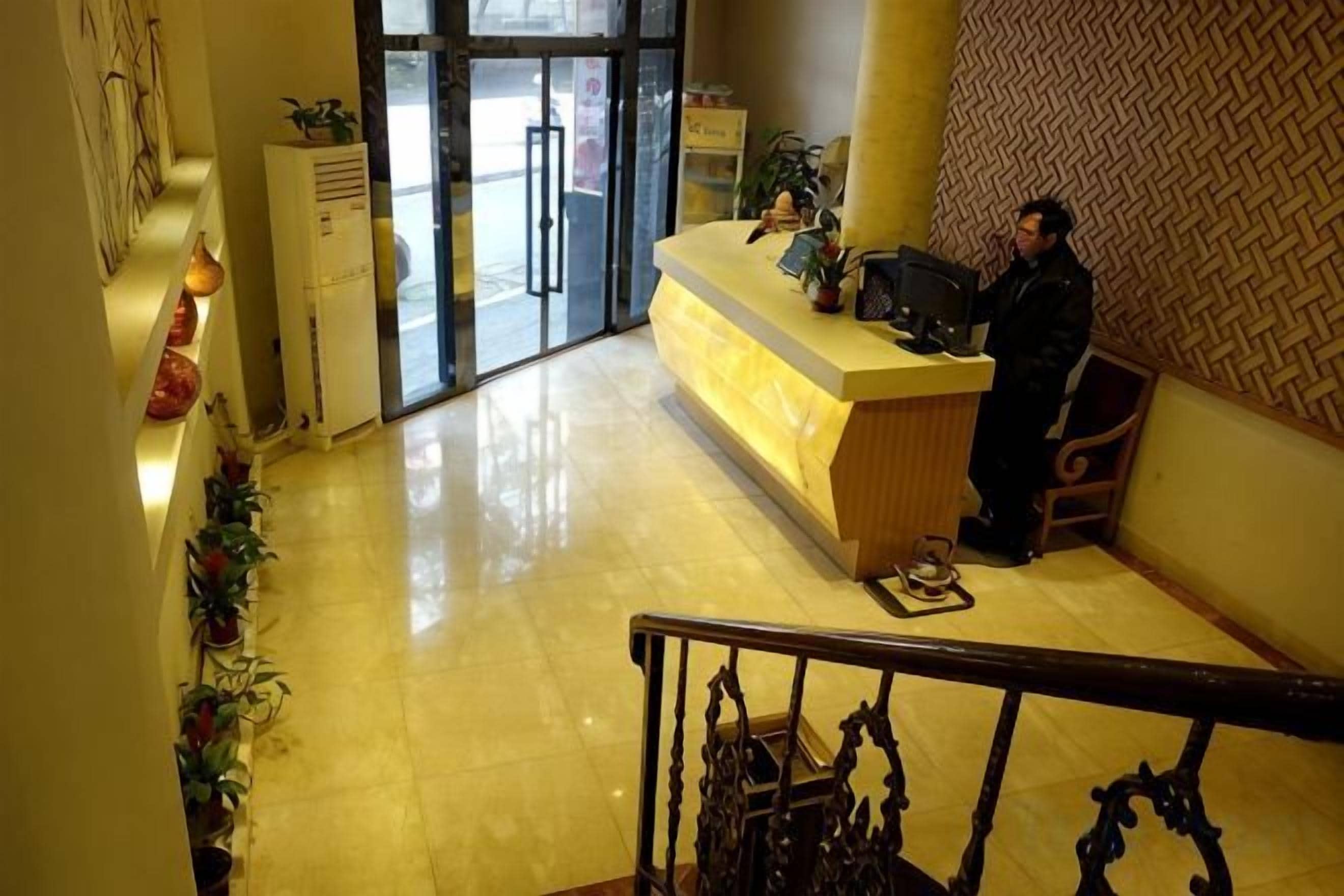 A hotel reception area with a reception desk, a staircase, and a patterned wall.