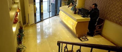 A hotel reception area with a reception desk, a staircase, and a patterned wall.