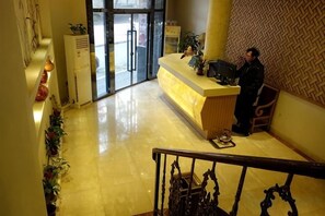 Un hall d'hôtel comprenant un comptoir d'accueil, un escalier et un mur décoré de motifs.