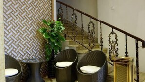 Una escalera con barandillas metálicas decorativas, una planta en maceta y sillas de mimbre con cojines.