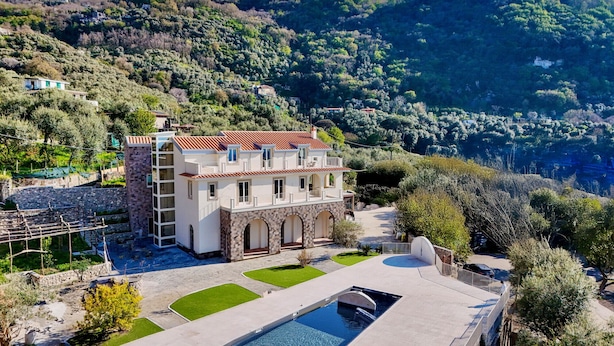 Una villa grande con piscina, rodeada de exuberante vegetación y colinas.