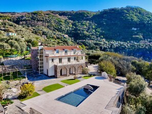 Une vaste villa dotée d’une piscine, entourée d’une végétation luxuriante et de collines.