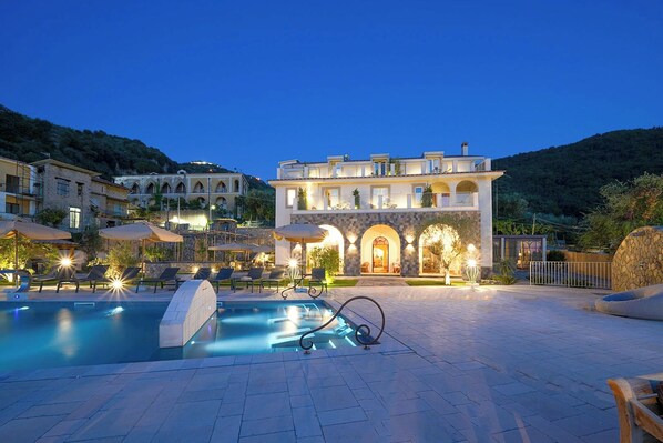 A hotel with a swimming pool, outdoor seating, and a well-lit entrance.