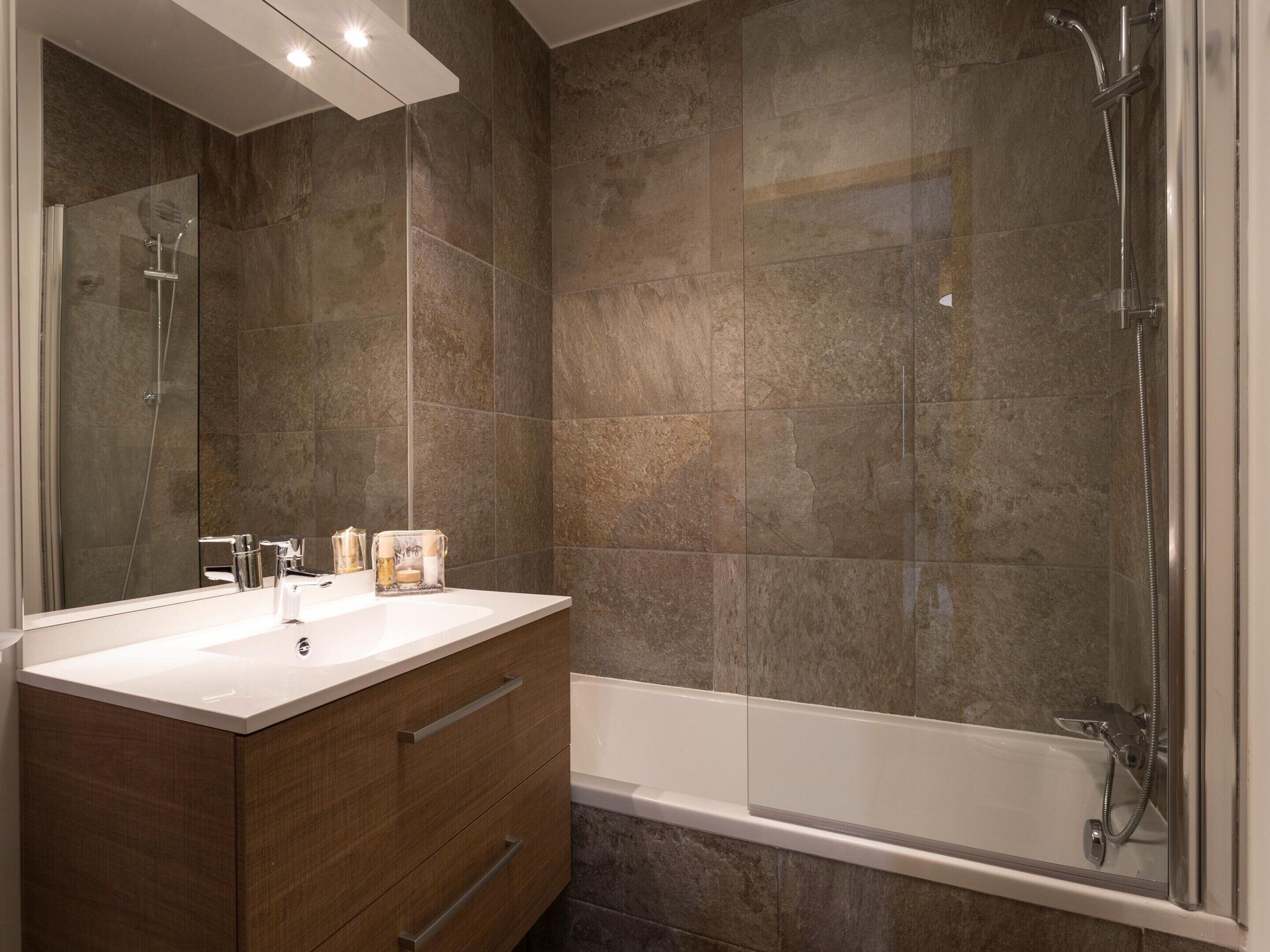 Un bagno moderno con un ampio specchio, un mobile bagno in legno, una vasca da bagno e uno spazio doccia.