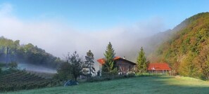 A house with a red roof surrounded by trees and a misty mountain backdrop. - Il Tesoro di Miro (Cartosio)