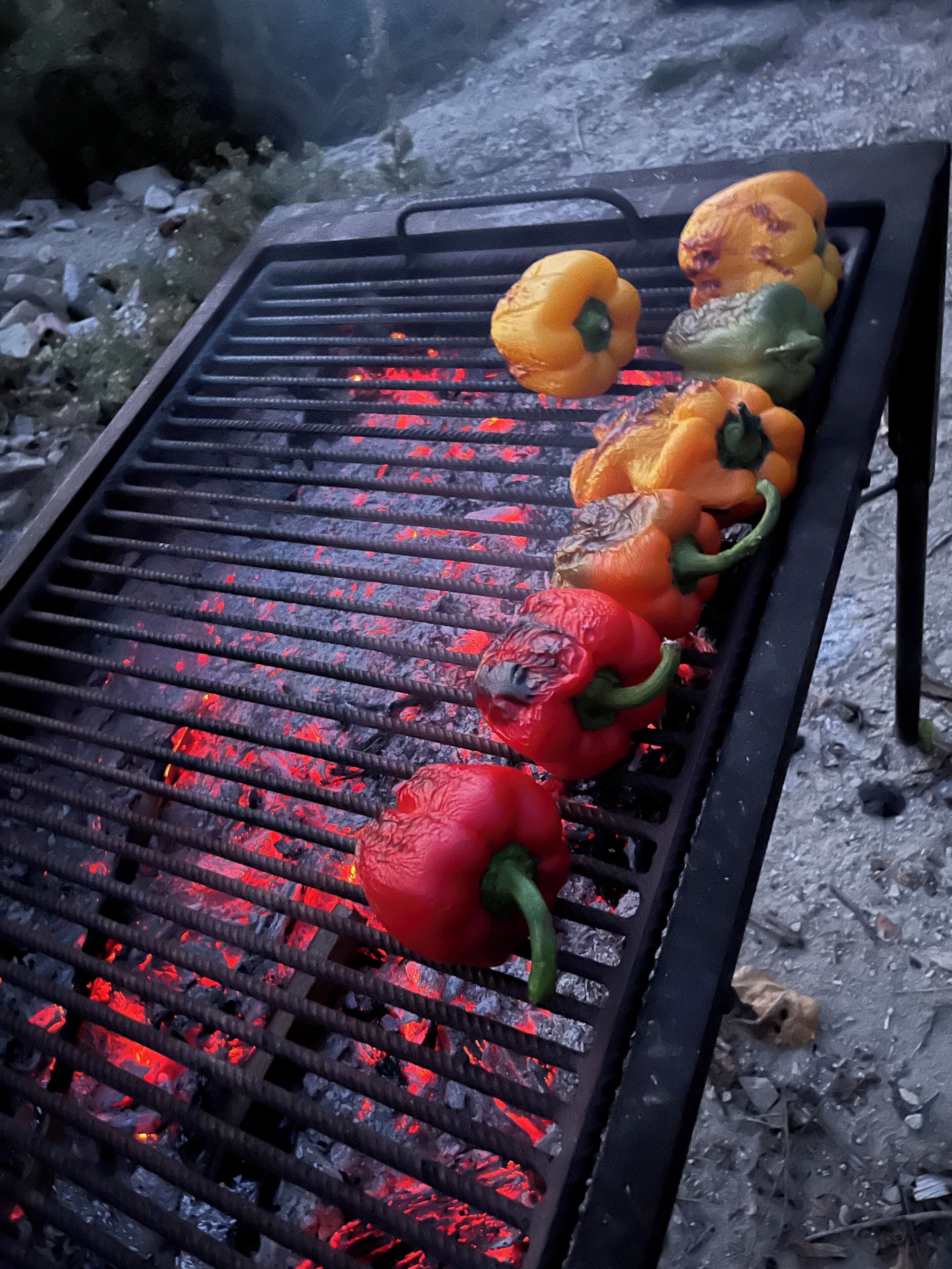 Ein Grill mit roten, orangen, gelben und grünen Paprika, die über offenem Feuer gegart werden.