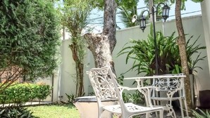 A courtyard with a white wrought-iron bench, a trash bin, and a tree. - Vivid Colombo (Colombo)