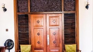 A spacious room with a large wooden door, two green upholstered chairs, a black chandelier, and a floor fan. - Vivid Colombo (Colombo)