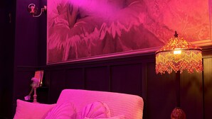 A room with a pink sofa, a round ottoman, a decorative lamp, and a wall mural. - Love room - La Villa 1900 - L'Instant X - Chic cocoon for a night for two (Chérancé)