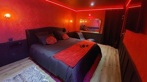 A modern bedroom with a large bed, red ambient lighting, a wooden floor, and a mirror above the bed. - Love room - La Villa 1900 - L'Instant X - Chic cocoon for a night for two (Chérancé)