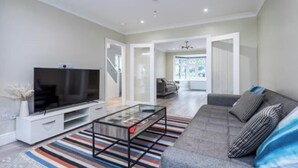 Un salon moderne avec un téléviseur à écran plat, une table basse en verre, un canapé gris et un tapis à rayures.