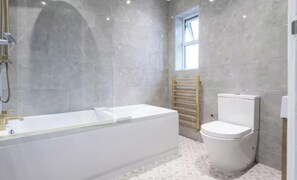 Une salle de bain moderne avec une baignoire blanche, des toilettes et une fenêtre laissant entrer la lumière naturelle.