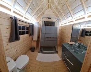 Une petite salle de bain en bois, aménagée dans une cabane, comprenant des toilettes, une douche et un lavabo.