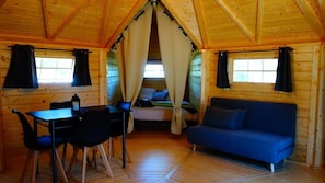 LâintĂ©rieur dâun chalet accueillant, avec un plafond en bois, un lit dotĂ© de rideaux, un canapĂ© bleu et une table entourĂ©e de chaises.