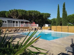 Une piscine avec une terrasse en bois, un espace clôturé et un bâtiment doté d’un patio couvert.