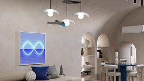 A modern living room with a sofa, a coffee table, and a dining area with chairs and a table. There is a wall-mounted light fixture and a wall art piece. - You & Me Cove Imerovigli (Imerovigli)