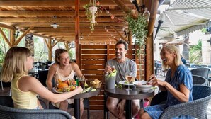 A wooden outdoor dining area with tables and chairs, surrounded by greenery and a covered structure. - ZEcamping 4* animé parc aquatique toboggans 500m plage locatif TV clim (Hyères)
