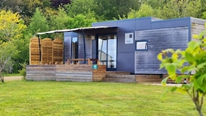 A modern cabin with a wooden deck, large windows, and a covered outdoor seating area. - ZEcamping 3 étoiles toboggans animaux acceptés locatif TV LV BBQ 32m2 (Loudéac)
