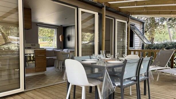 Un espace repas extérieur avec une table et des chaises en verre, une terrasse en bois et une vue sur le jardin arrière.
