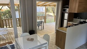 Une cuisine compacte équipée d’un four à micro-ondes, d’une cuisinière et d’un évier. On y trouve également un coin repas avec une table et des chaises, ainsi qu’une terrasse avec une plateforme en bois et des meubles d’extérieur.