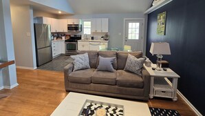 A modern living room with a brown sofa, a glass coffee table, and a white side table with a lamp. - Beautiful Bray Cottage on the Vineyard (West Cape May)
