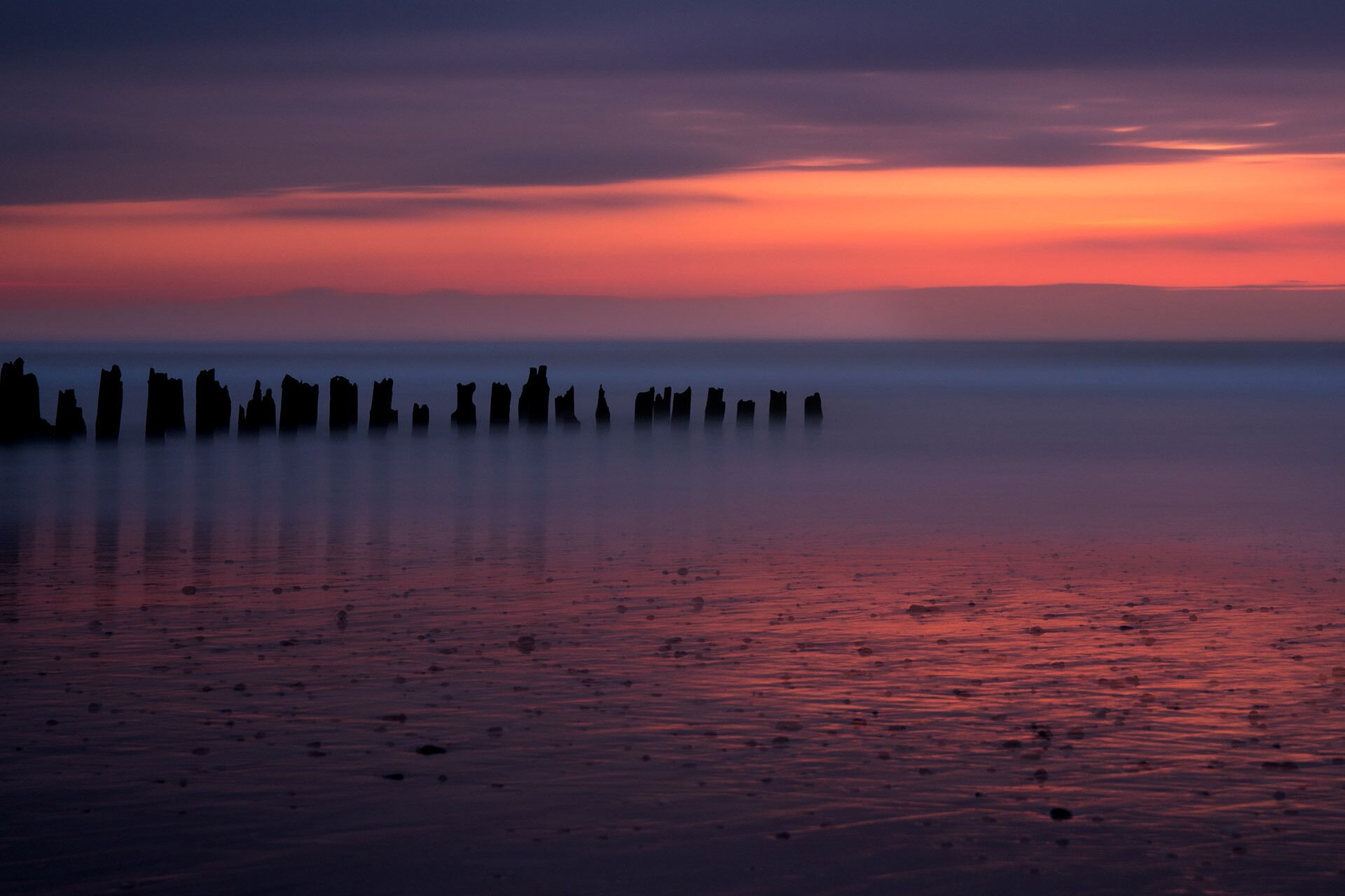A beach with rock formations silhouetted against a sunset.
