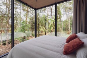 A bedroom with a large window, a bed with white linens and two pillows, and a view of a forested area. - BonjourSauvage Seignosse  (Seignosse)