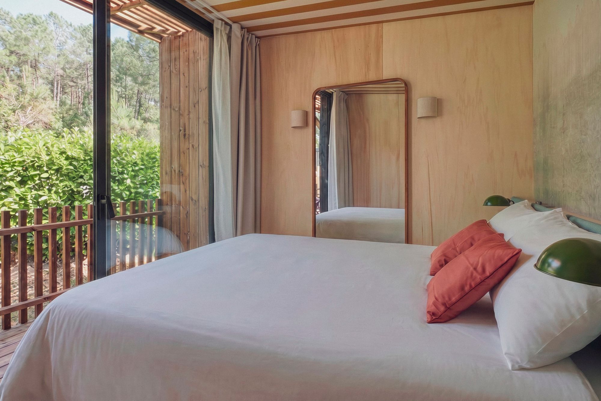 A bedroom with a large bed, a wooden ceiling, a window with curtains, and a view of greenery outside.