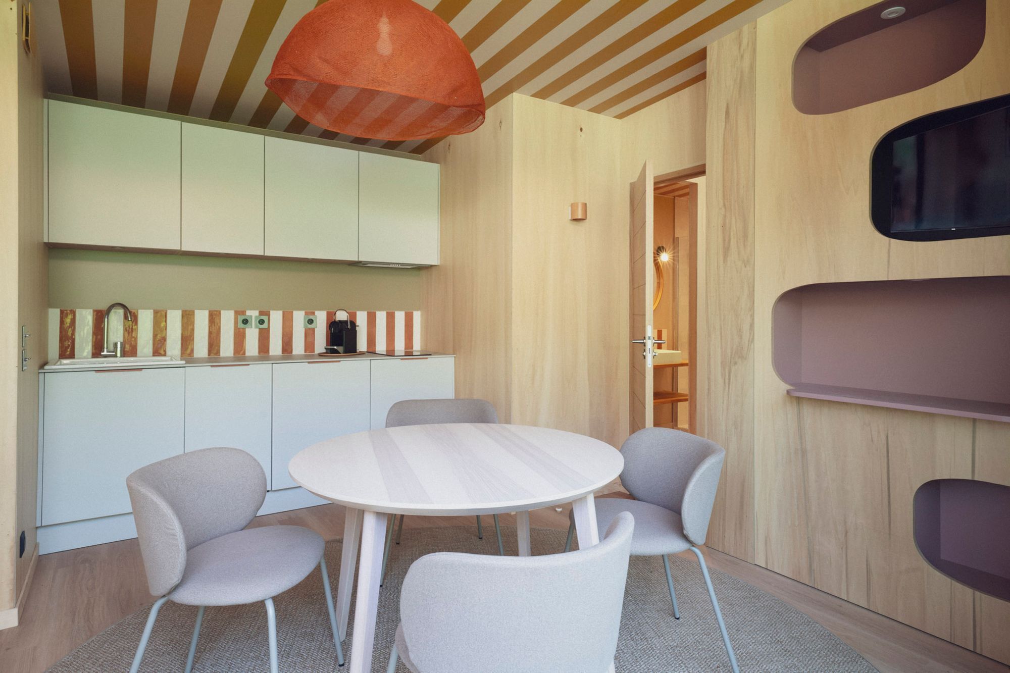 A modern kitchen with a round table and four chairs, wooden cabinets, and a striped backsplash.