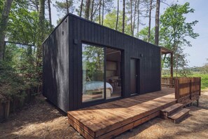 Eine moderne Holzlaube mit Terrasse, großen Glasfenstern und einer Tür zu einem Innenbereich.