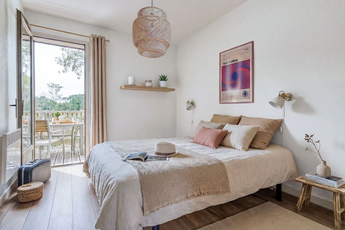 A bedroom with a bed, bedside table, lamp, and a view of the outdoors.