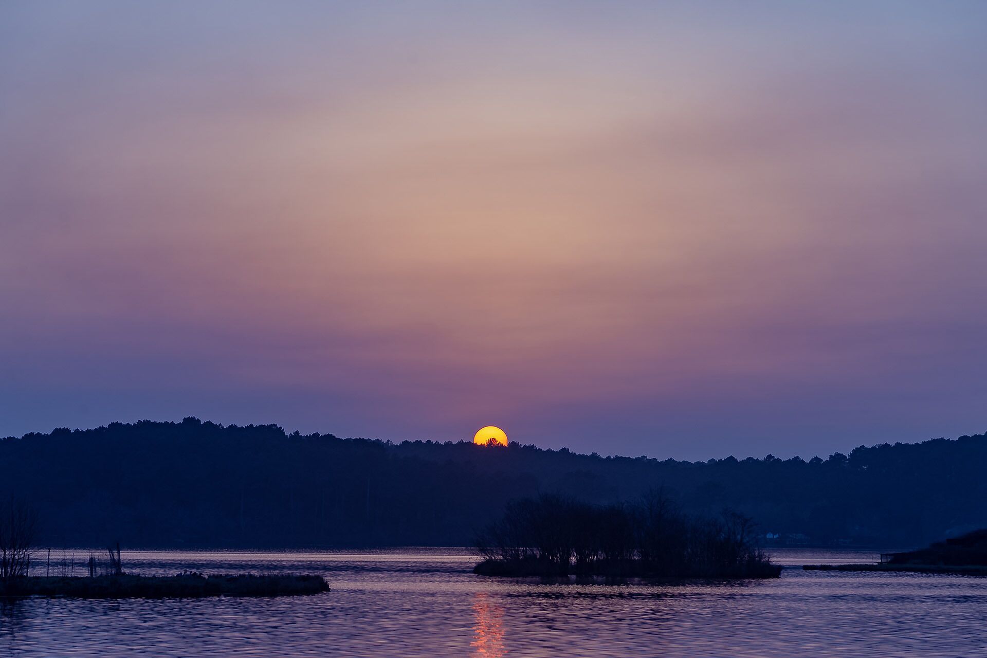 A sunset over a calm body of water with a distant landmass and a small island.