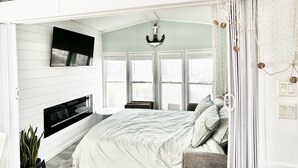 Ein Schlafzimmer mit Bett, Wandfernseher und einem Vorhangfenster.