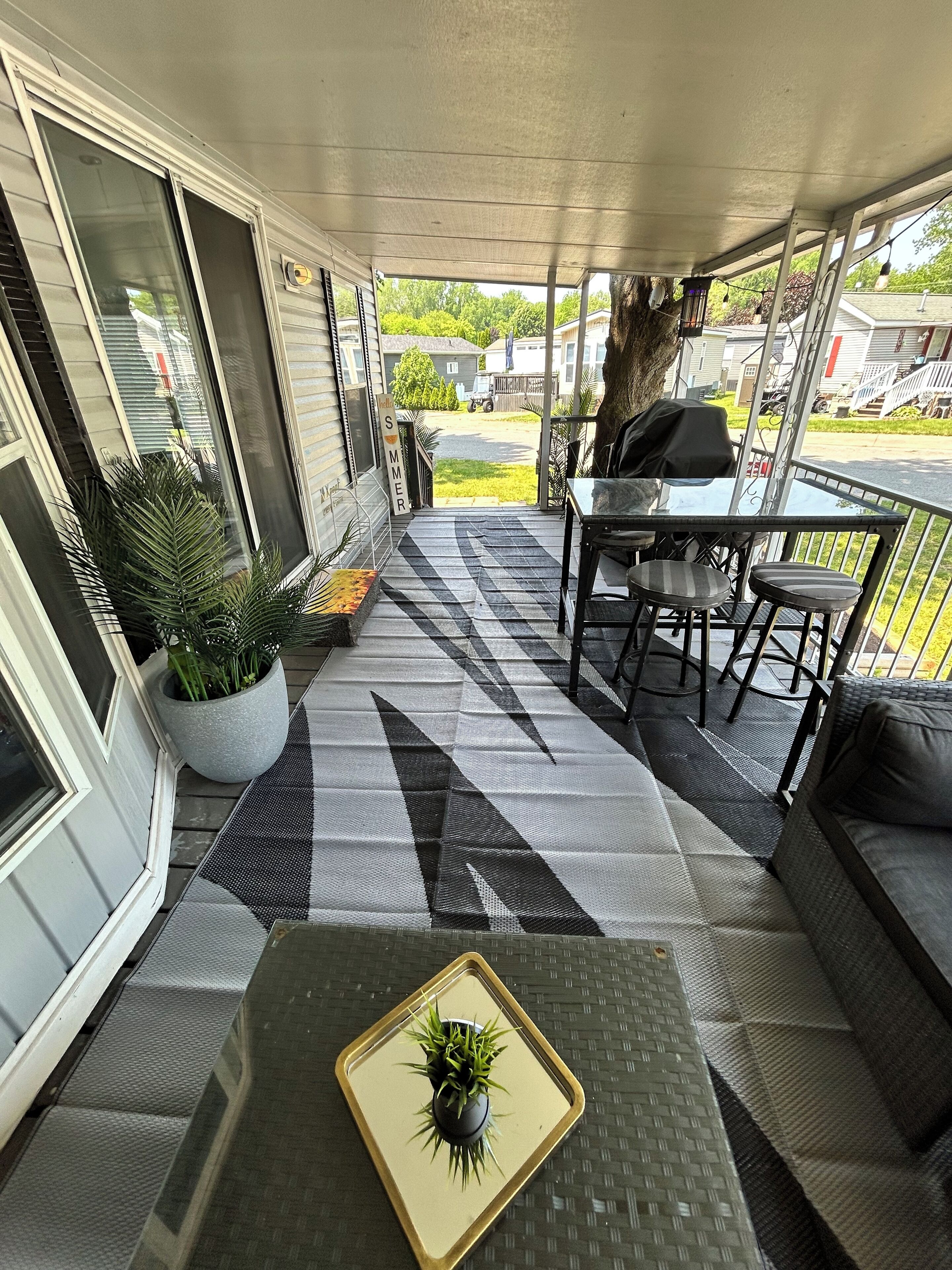 A covered patio area with a table and chairs, potted plants, and a view of the neighborhood.