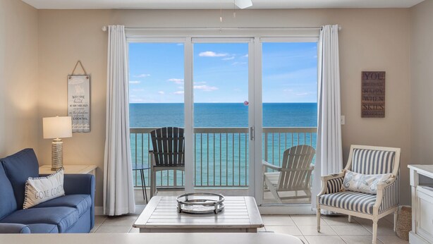 A room with a view of the ocean, a ceiling fan, a table with a tray, a blue sofa, and striped chairs.